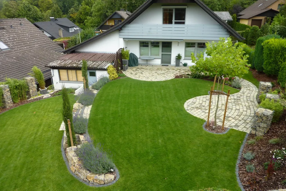 Neu angelegter Garten mit geschwungener Rasenfläche, gepflastertem Weg und frisch bepflanzten Beeten